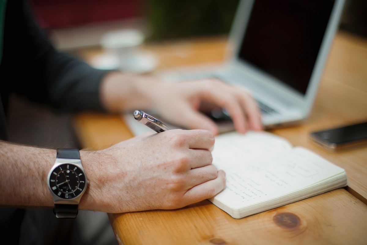 man sitting while writing on notebook