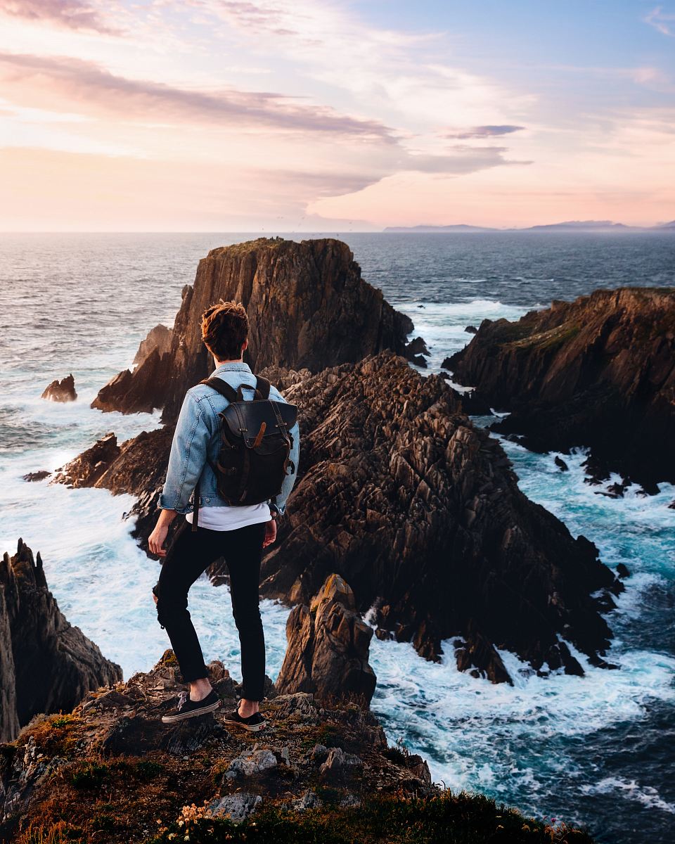 man standing near cliff looking at body of water during daytime