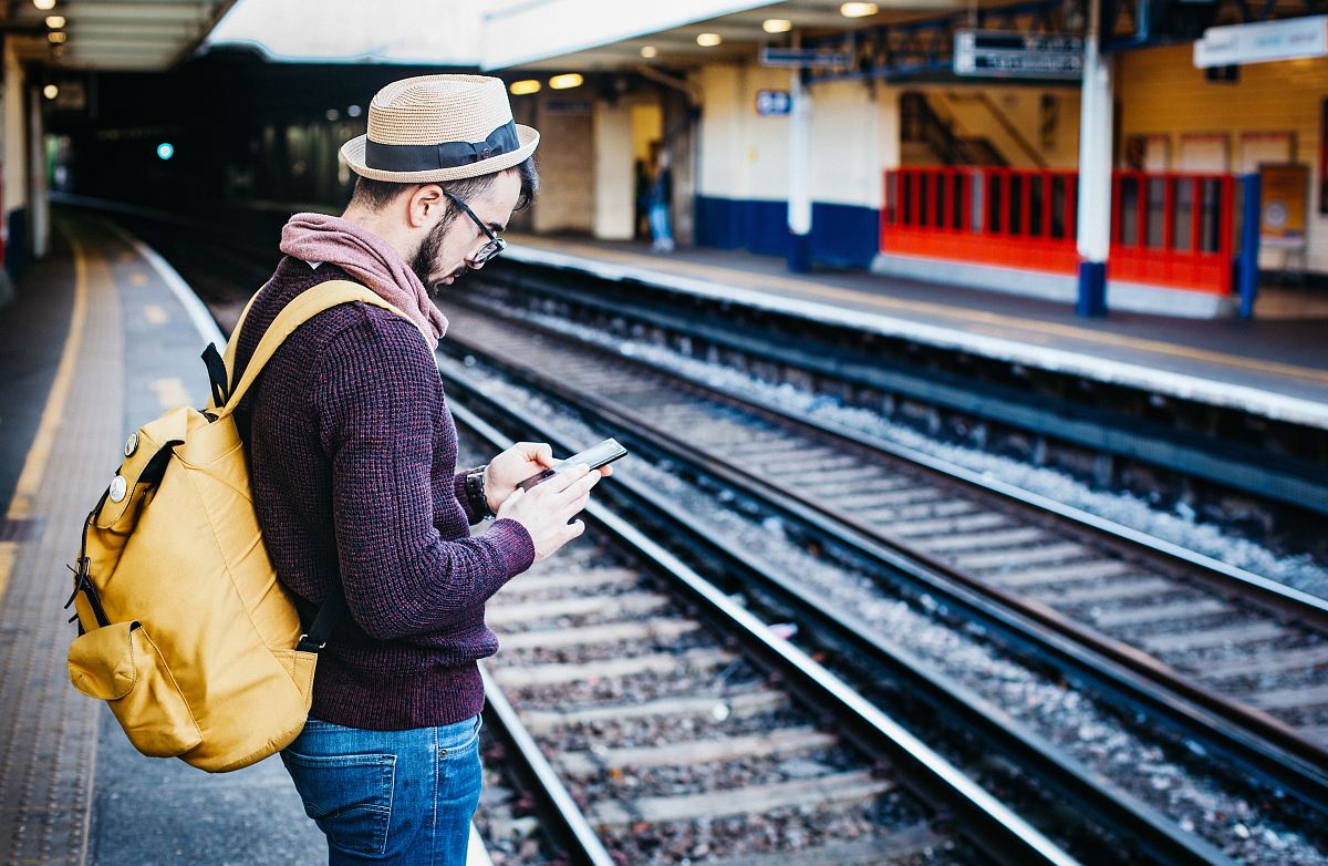 man using phone while standing in front of train rail during daytime