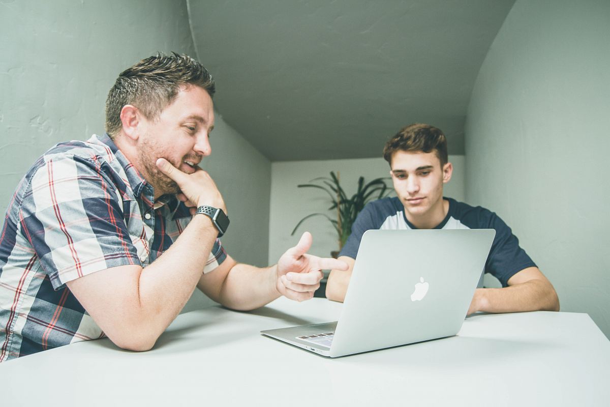 man wearing white and black plaid button-up sports shirt pointing the silver MacBook