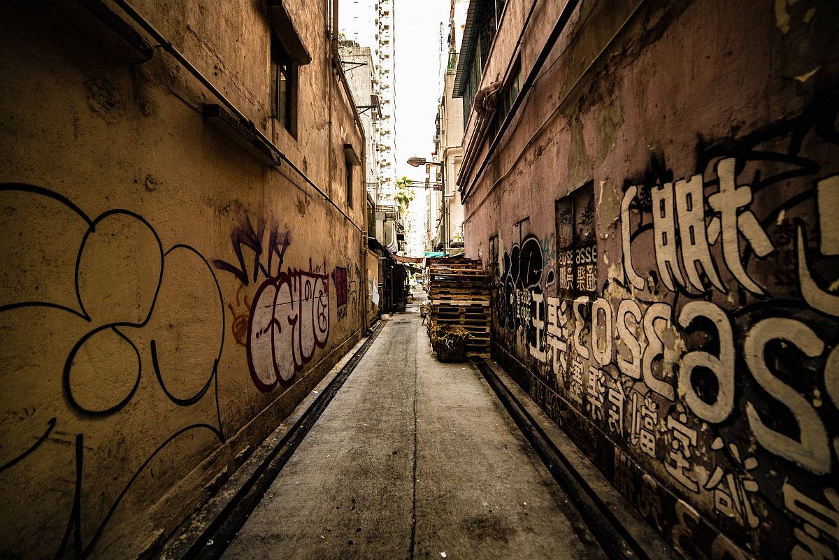 Explore the vibrant essence of urban life with this captivating image of a narrow alleyway adorned with colorful graffiti, set beneath a dramatic white sky. This scene captures the raw energy of city streets, making it perfect for use in projects related to street art, urban culture, or lifestyle photography. Ideal for marketers, bloggers, and designers looking to evoke a sense of edgy creativity.