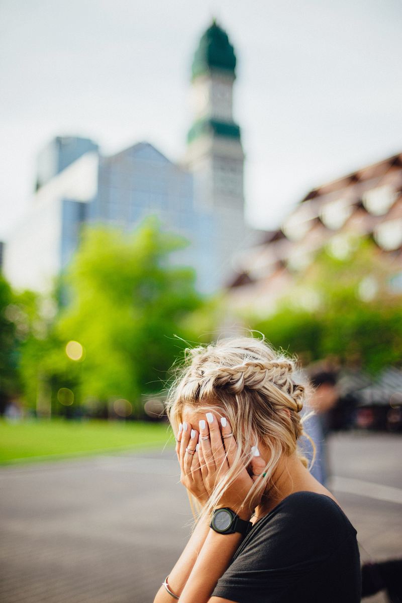 person covering face with hands outdoors
