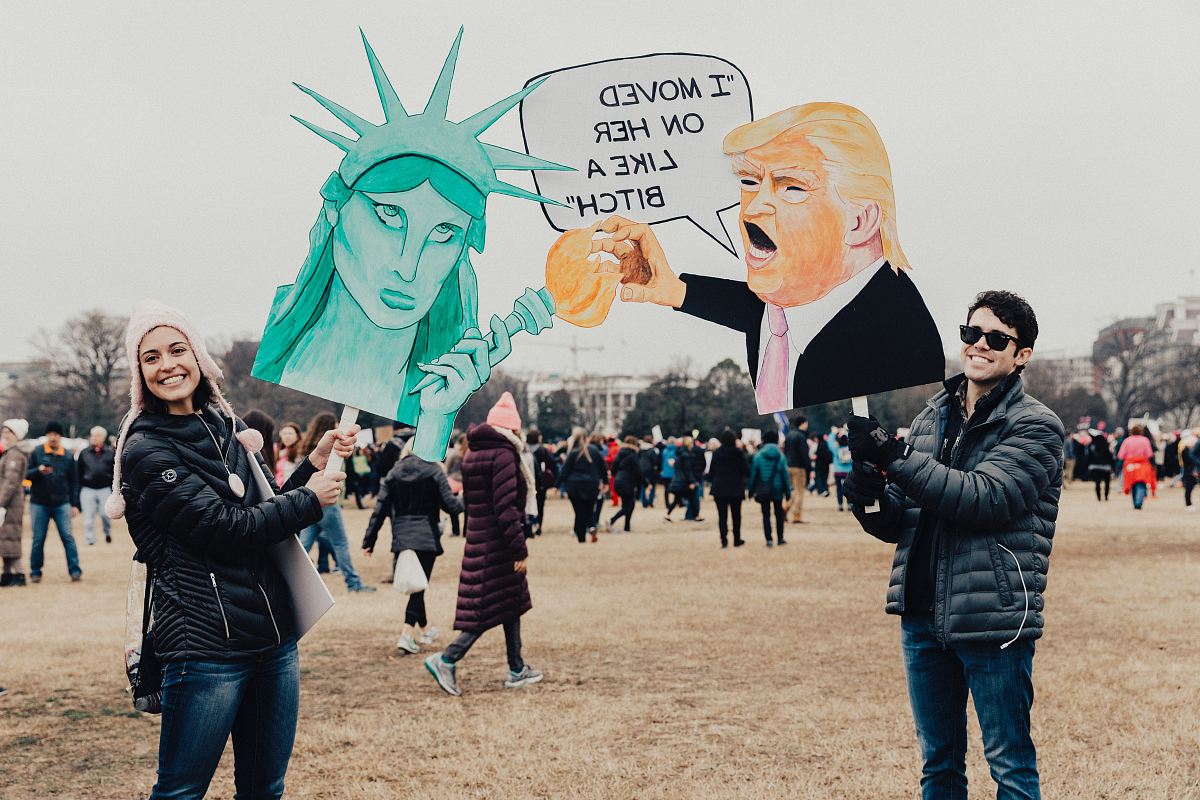 person wearing black bubble jacket holding donald trump signage