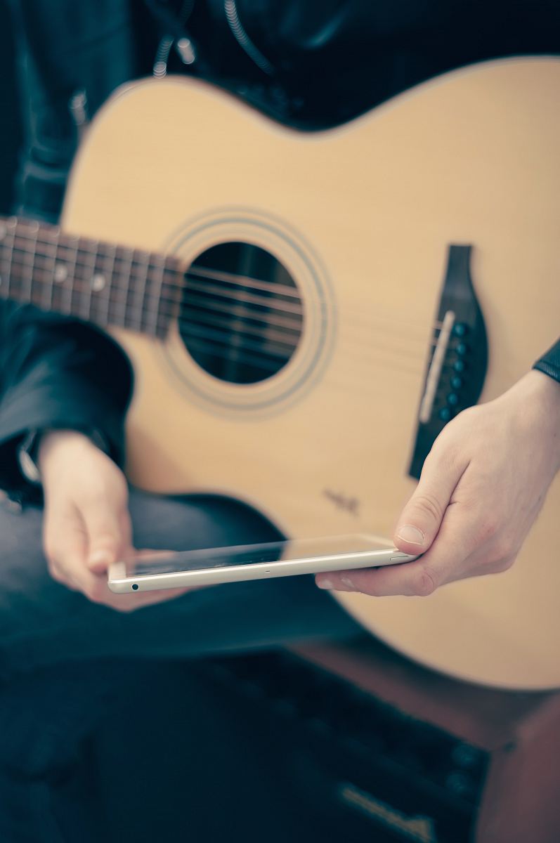person with guitar on lap holding tablet