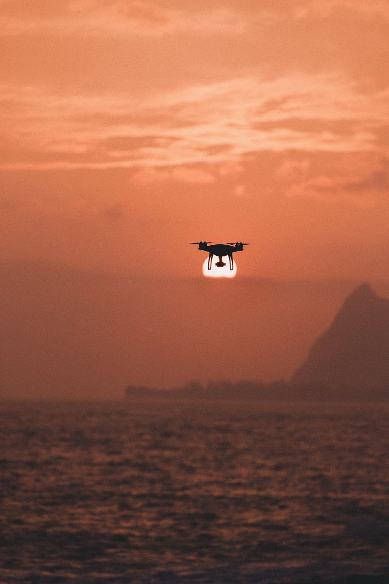silhouette of drone hovering above body of water