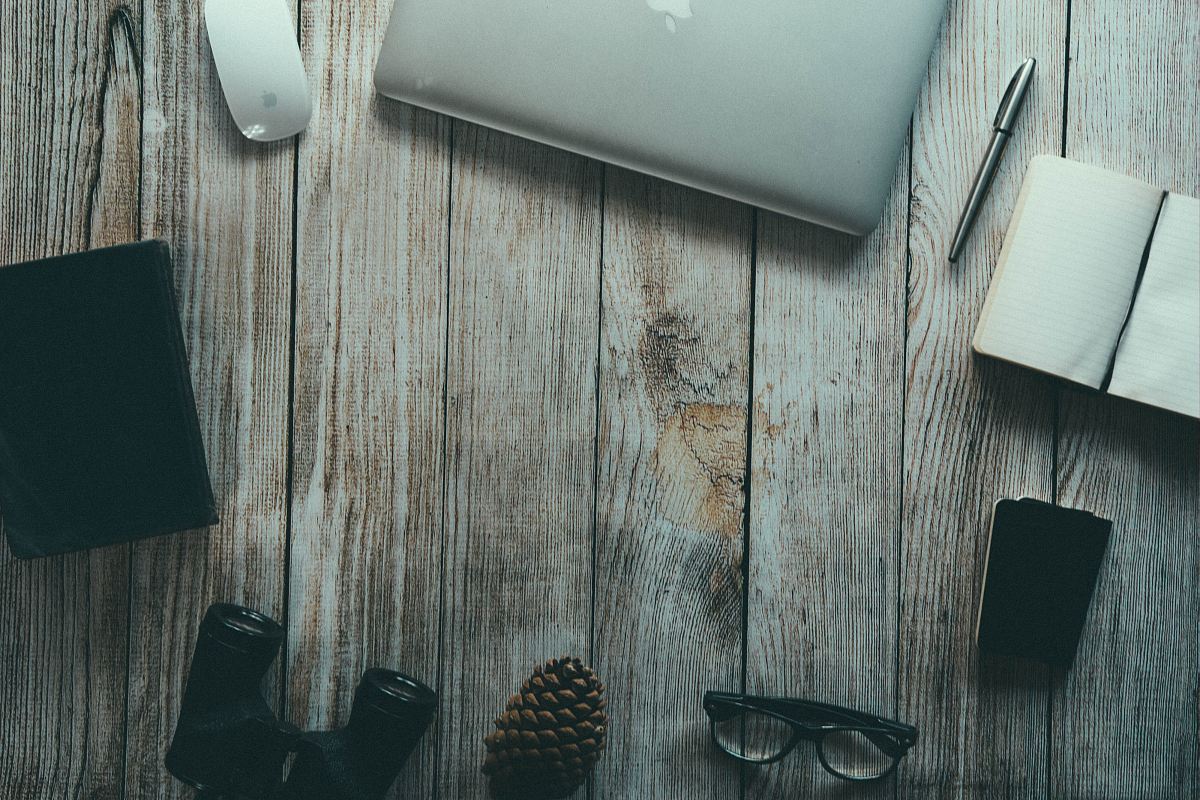 silver MacBook, ballpoint pen, binoculars, eyeglasses arranged in circular pattern