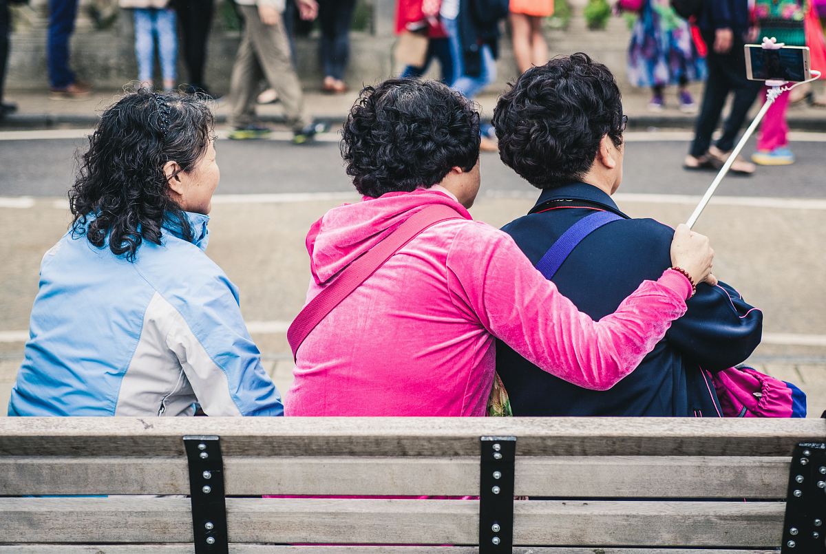 This lively scene features three friends enjoying a sunny day at the park, comfortably seated on a bench as they take a selfie together. The joy and camaraderie of their shared moment is palpable, making this image perfect for lifestyle blogs, social media campaigns, or promotional materials that highlight friendship, leisure, and outdoor activities. The vibrant daytime setting adds an element of warmth and positivity, ideal for capturing the essence of joyful moments.