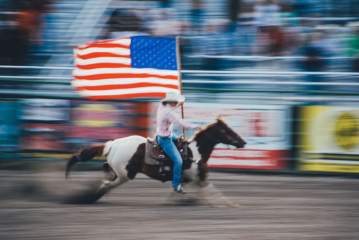 time lapse photo of man carrying U.S. flag while riding brown horse