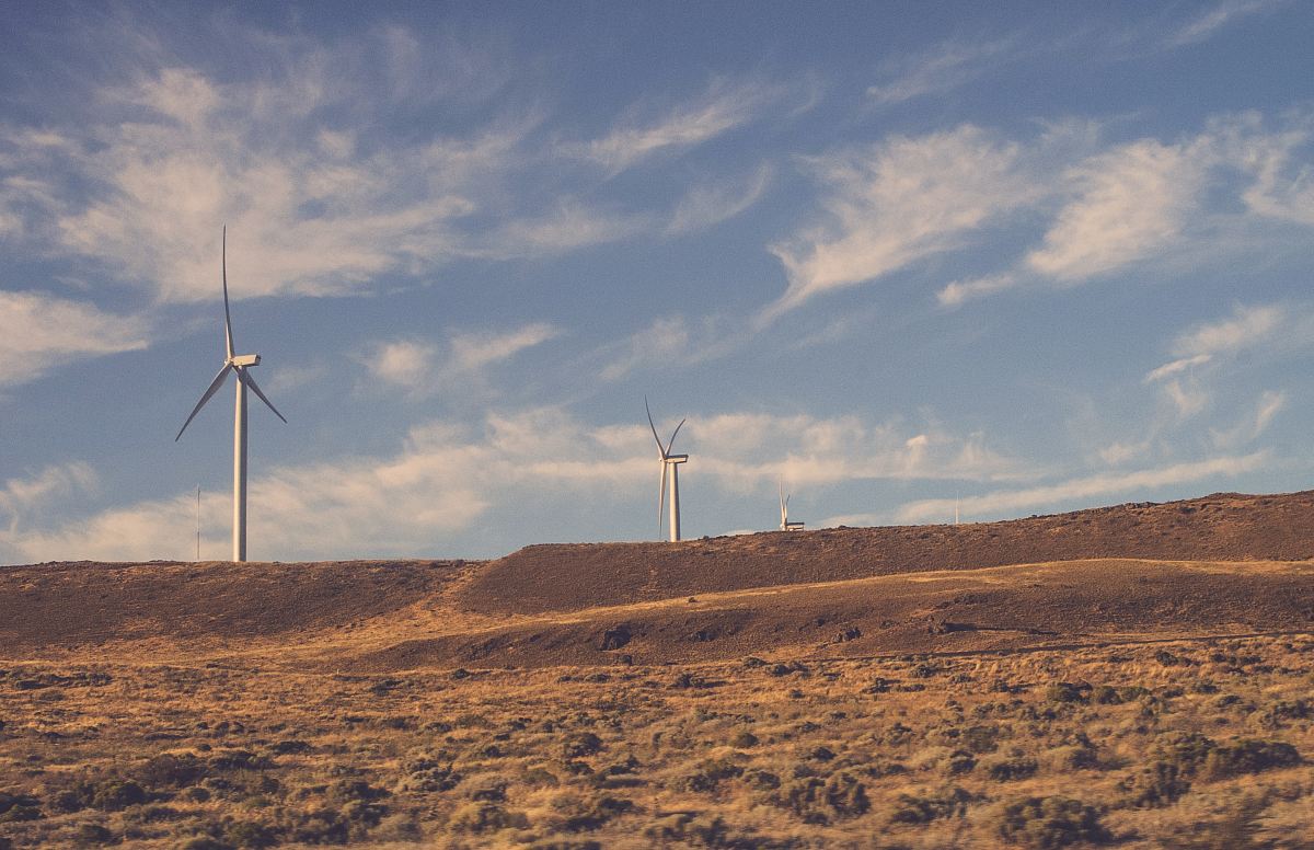 two gray wind turbines under cloudy blue sky during daytime