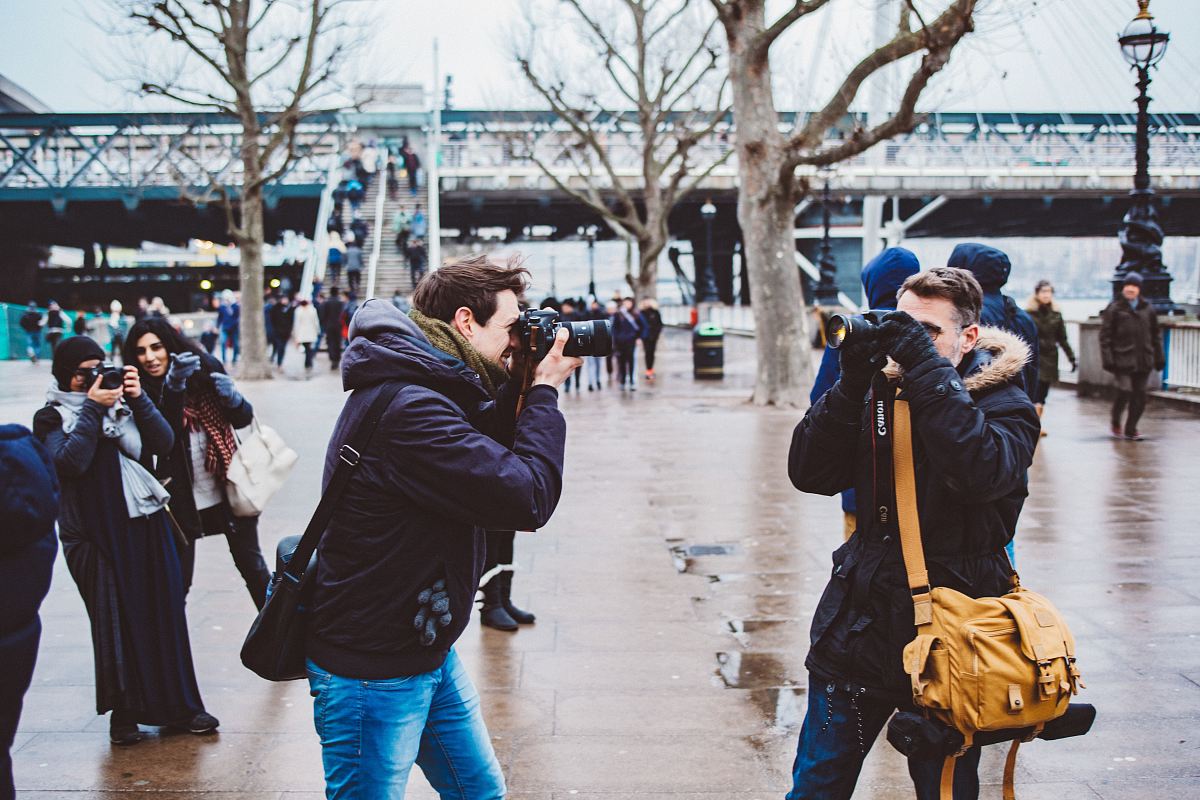 two men facing each other taking photo in black DSLR camera during daytime