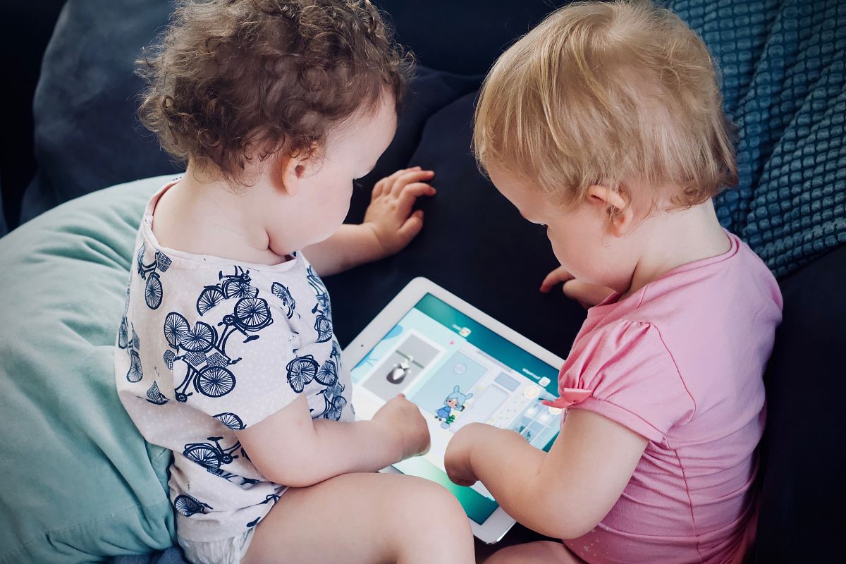 two toddlers sitting on sofa while using tablet computer