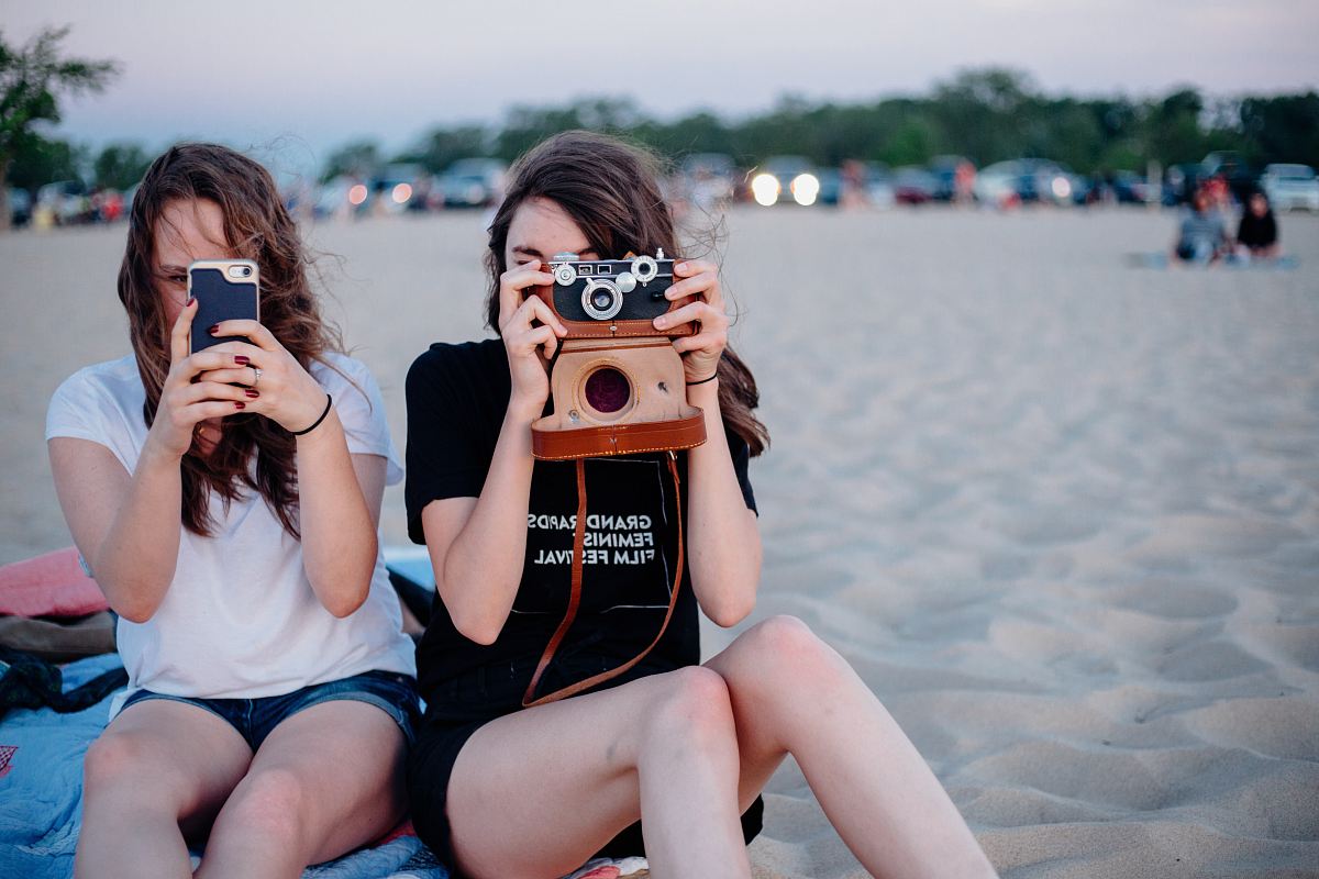 two woman taking photos using smartphone and camera