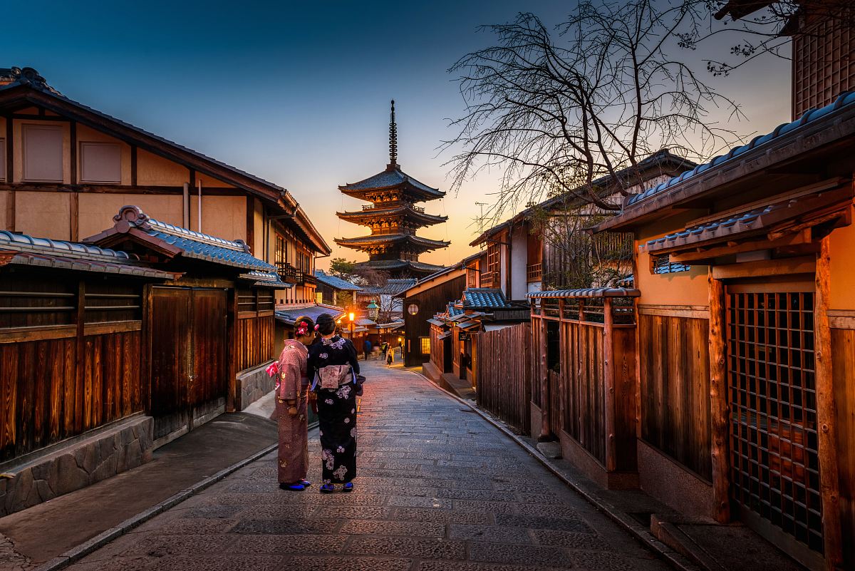 two women in purple and pink kimono standing on street