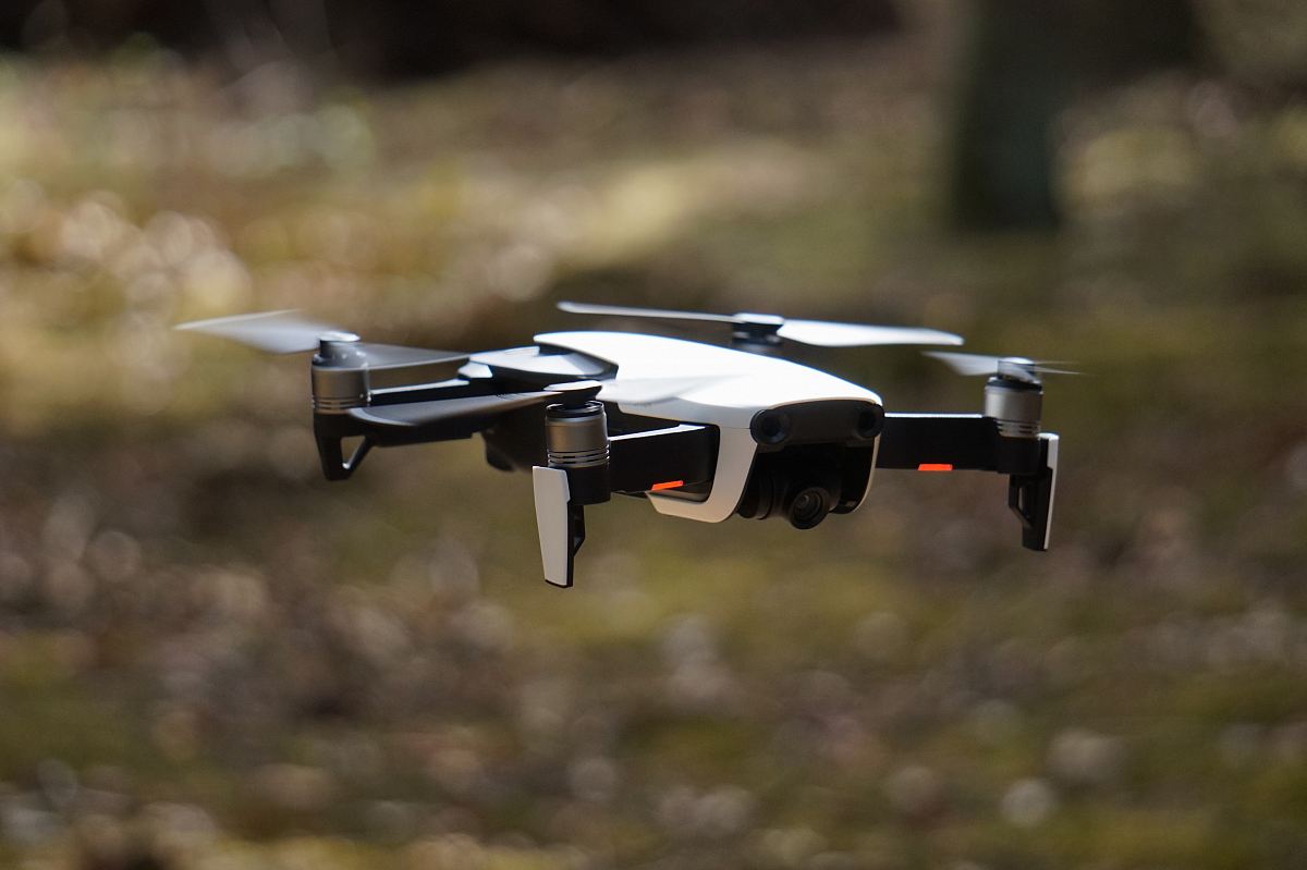 white and black quadcopter hovering on grass