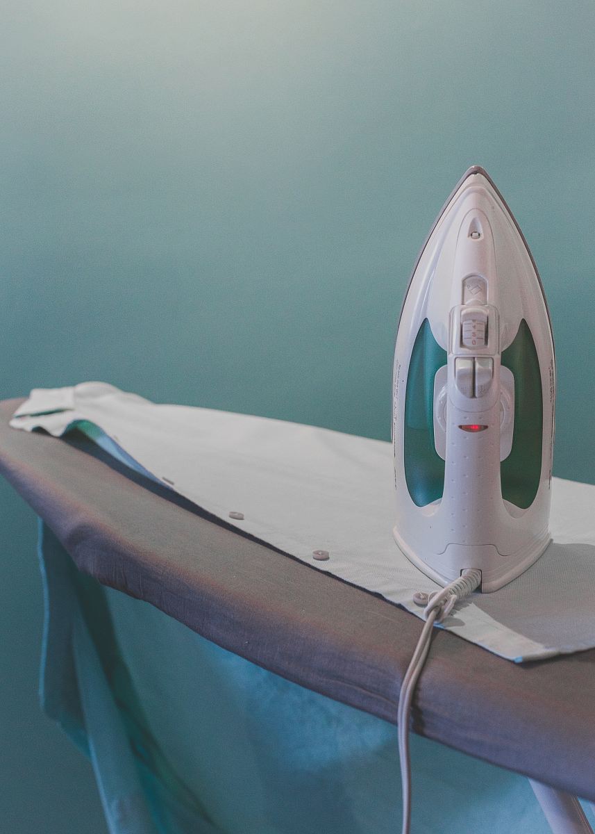 white and teal steam clothes iron plugged on ironing board