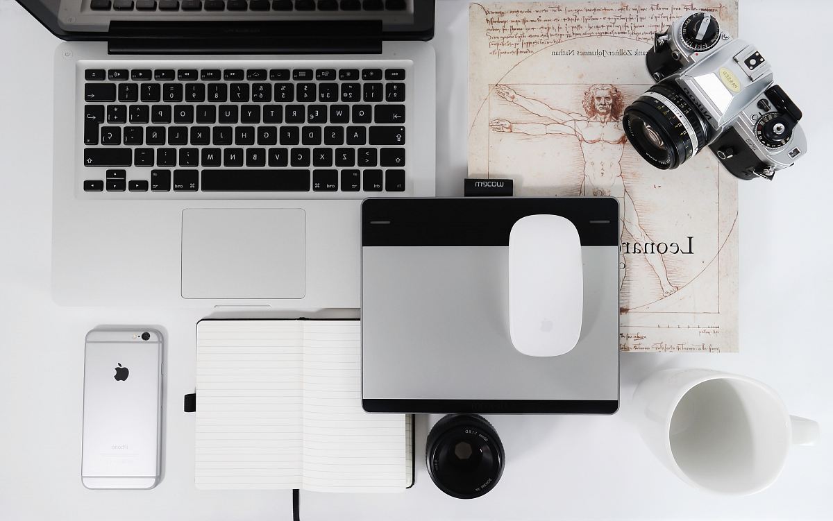 white Apple Magic Mouse, gray trackpad, gray SLR camera, space gray iPhone 6s, and MacBook Pro on table