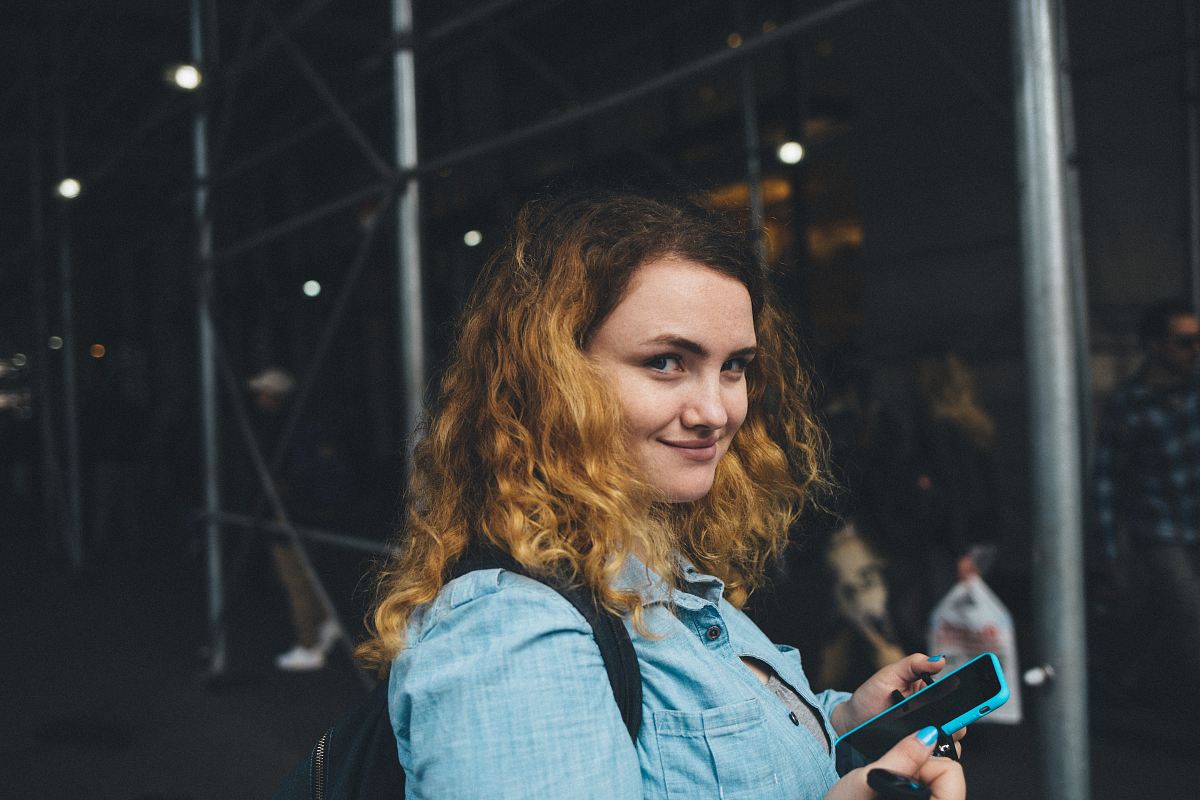woman holding black smartphone near gray metal frame at daytime