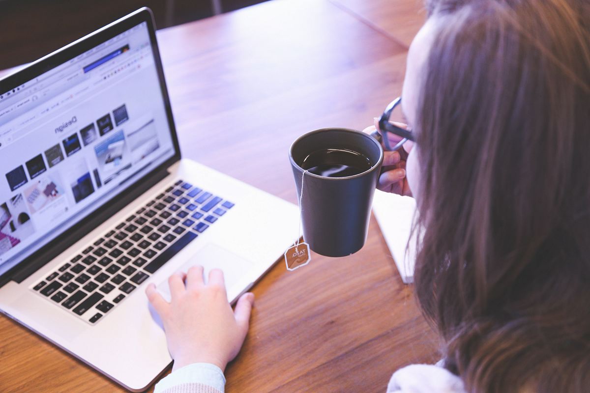 woman holding tea filled mug using MacBook