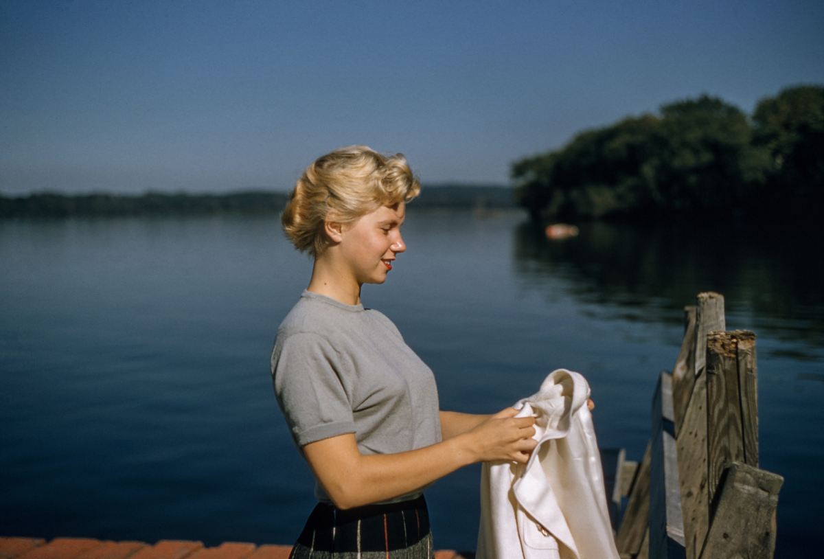 woman holding white textile standing beside body of water