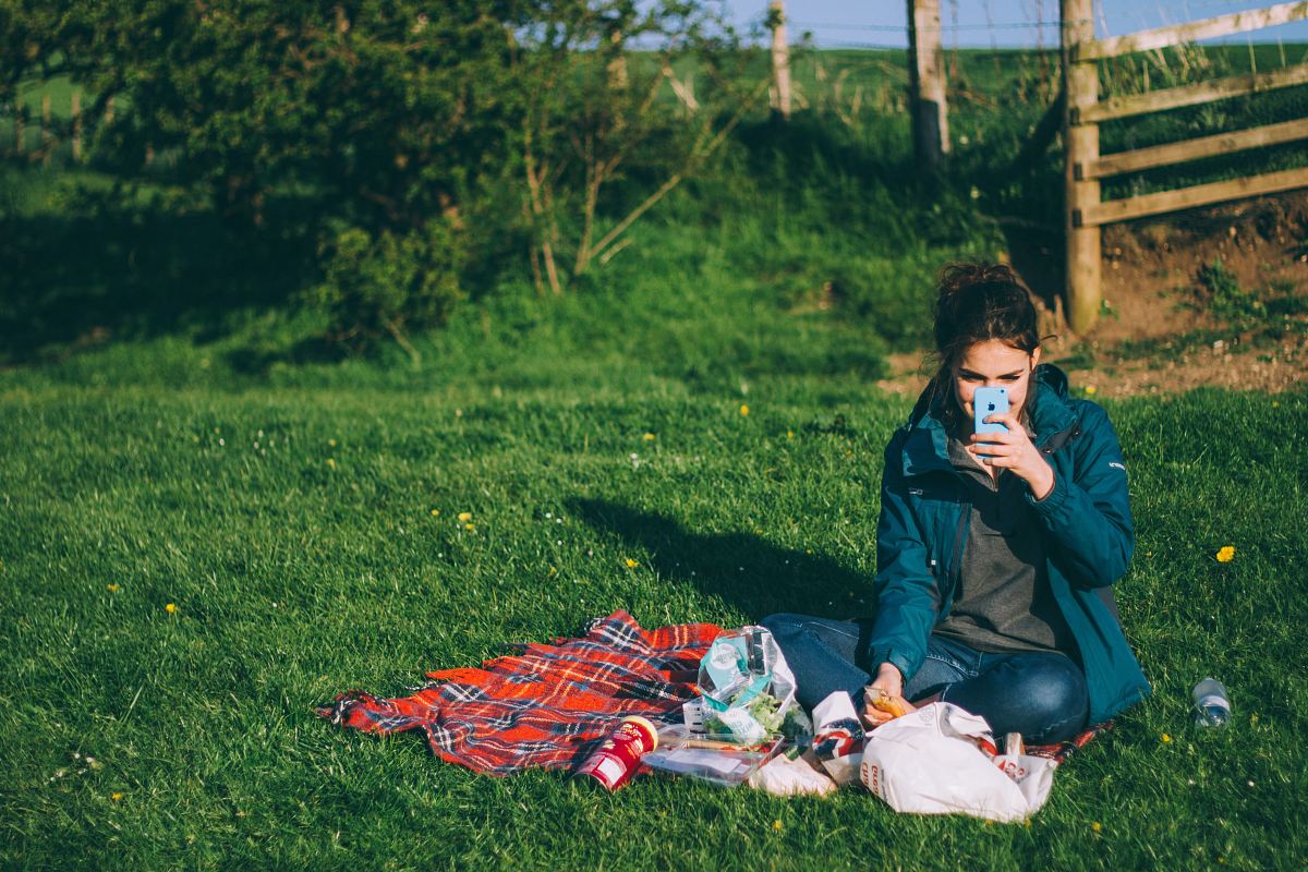 woman in blue outfit using blue smartphone while sitting on grass