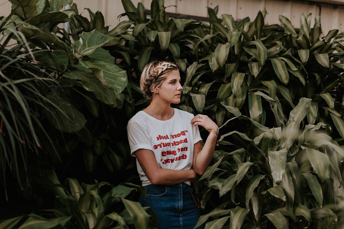woman in white shirt standing and surrounded by green plants