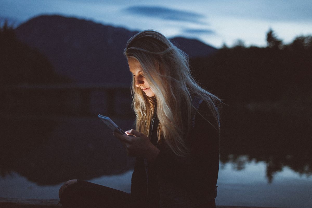 woman looking at phone beside body of water