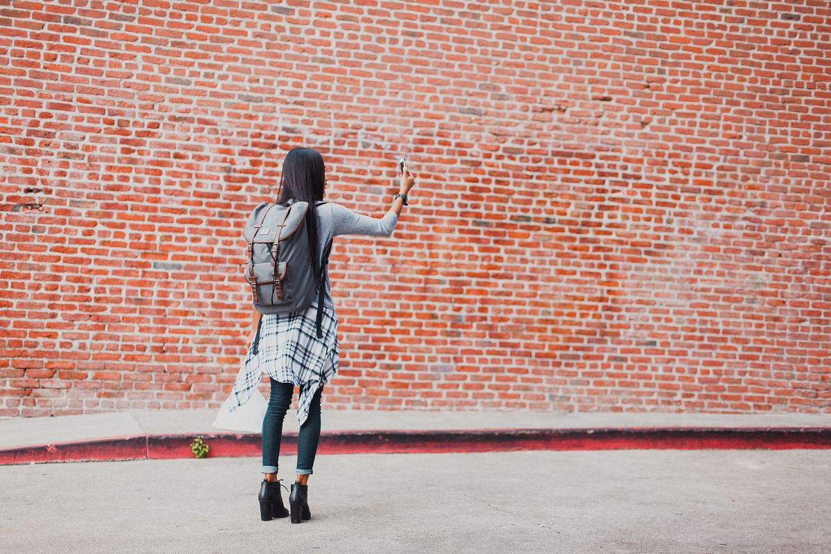 woman standing beside cinder brick wall while using smartphone