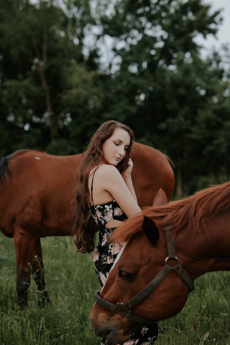 woman standing between brown horses at daytime