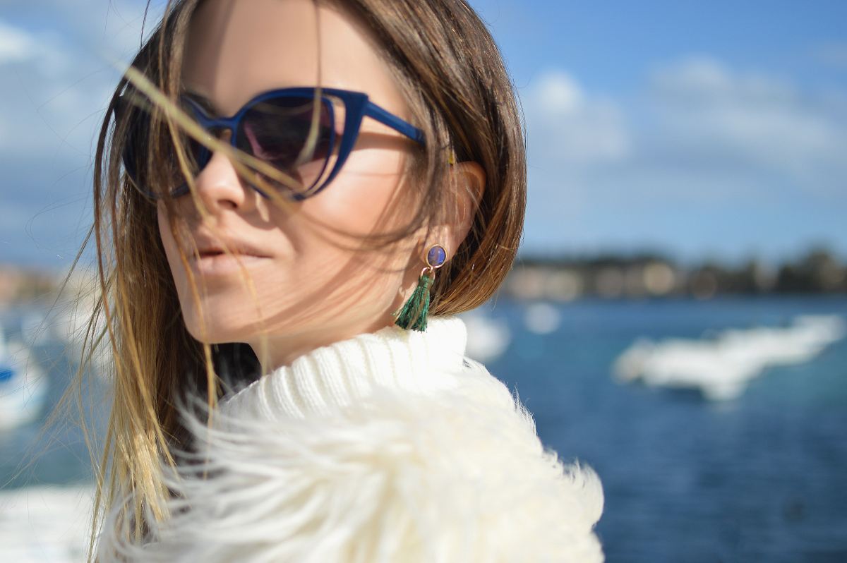 woman wearing blue-framed cat-eye sunglasses with body of water background