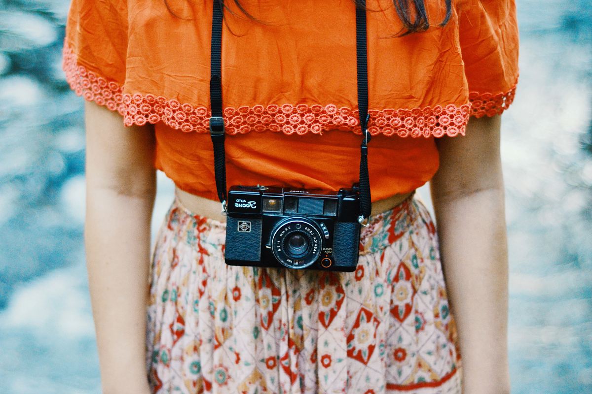 woman wearing orange and multicolored dress with black bridge camera on her neck