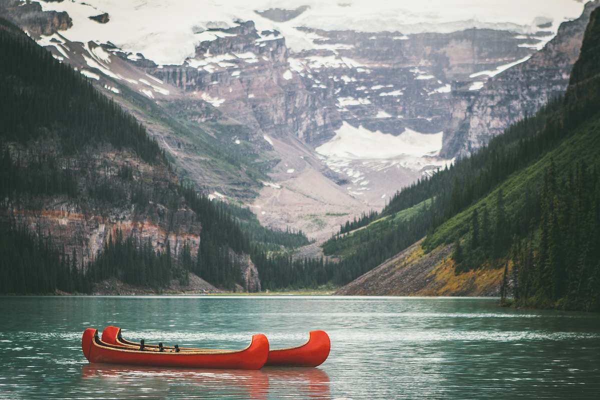 mountain two orange boats on body of water in front of mountain with trees during daytime canoe