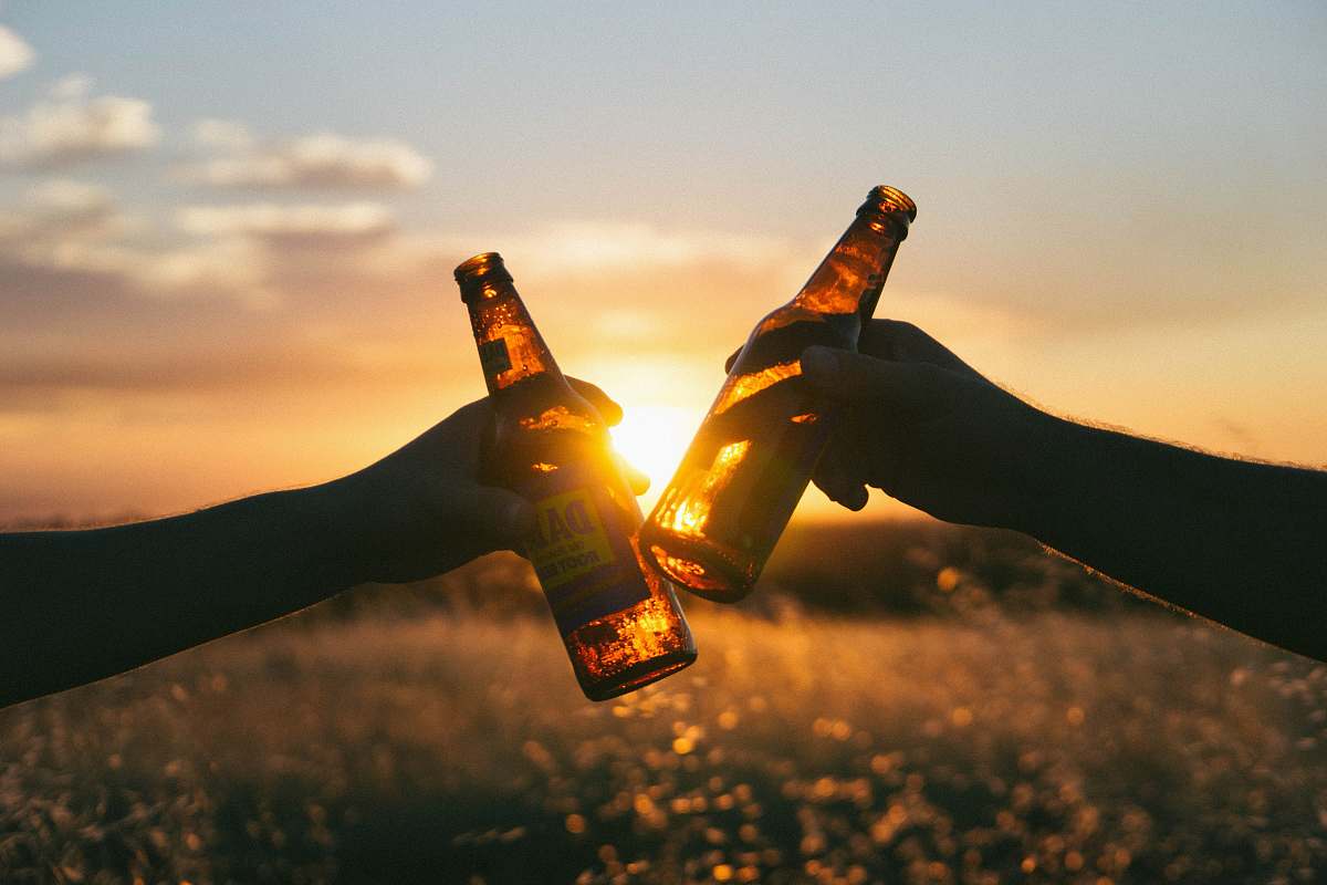 bottle photography of person holding glass bottles during sunset sunset
