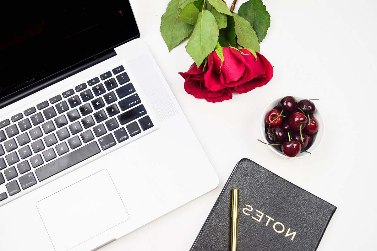 hardware flatlay photo of rose, MacBook Pro, cherries, and black notebook computer keyboard