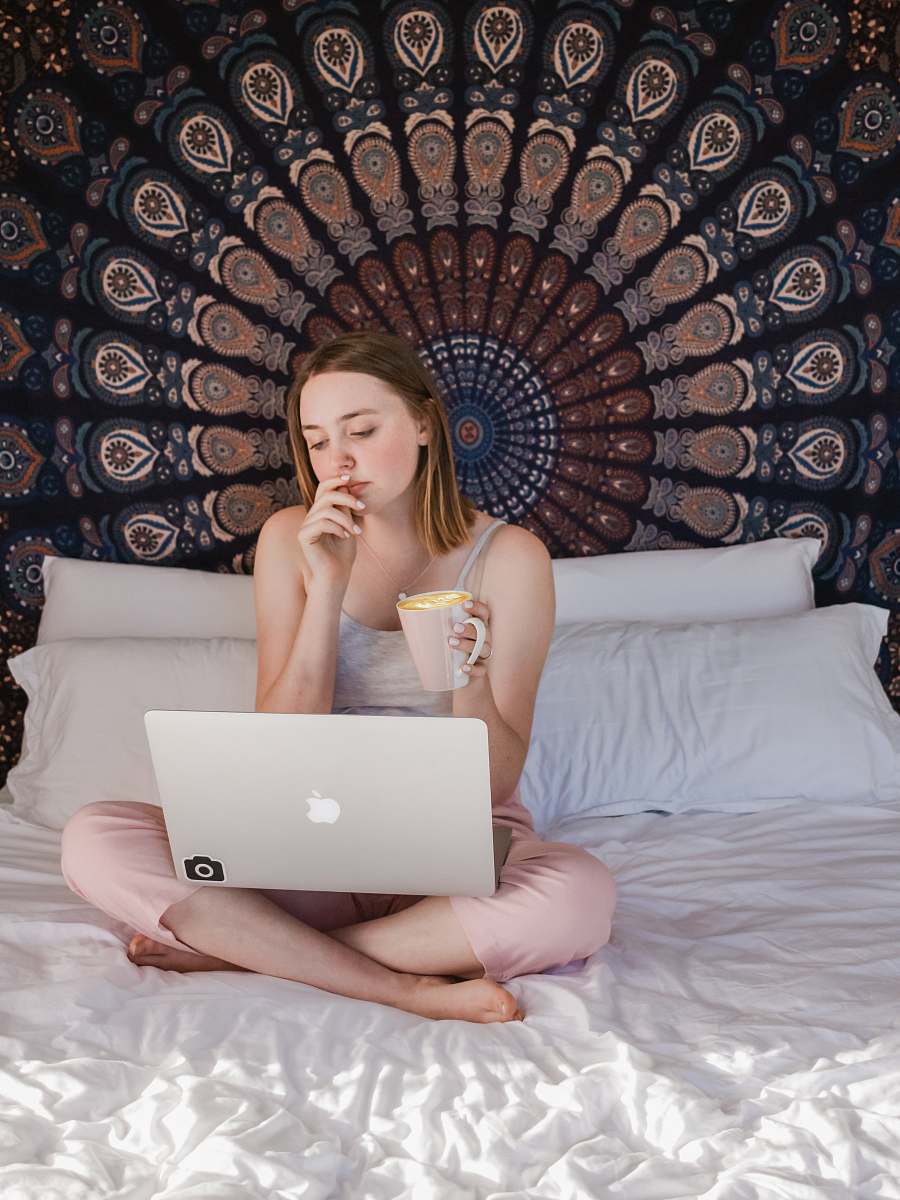 electronics woman using MacBook and holding mug while sitting on bed pc