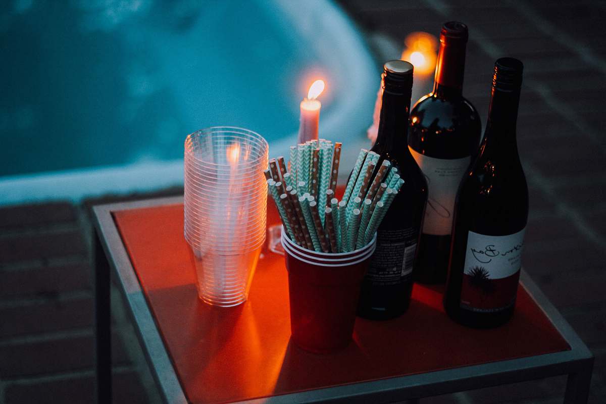 bottle three wine bottles near cup and candle on square red table redding