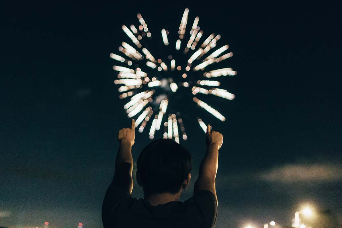 night man in black shirt pointing towards brocade fireworks in the skies firework