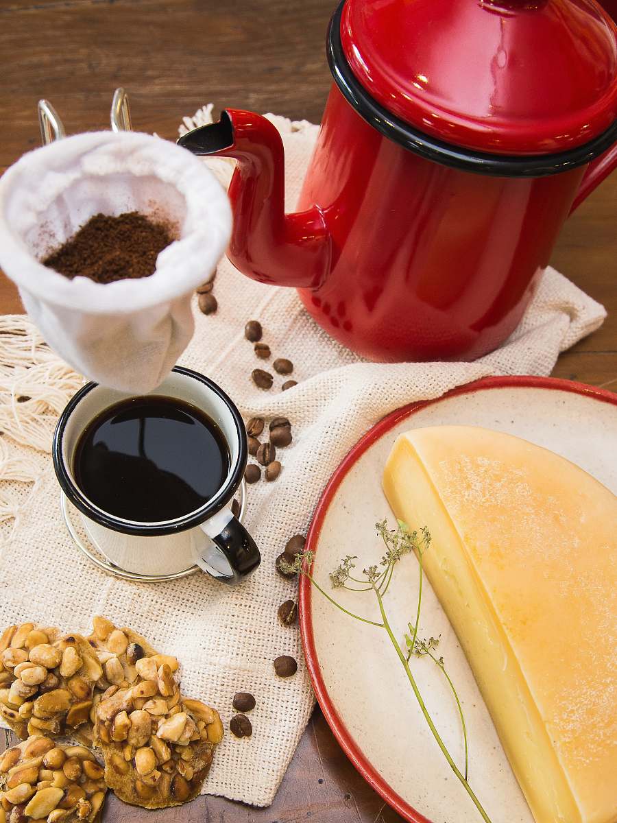 fondue red and black kettle near mug filled with coffee and half a cheese on table state of minas gerais