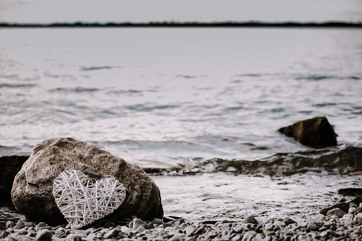 sea heart-shaped string artwork leaning on brown rock near shoreline at daytime water