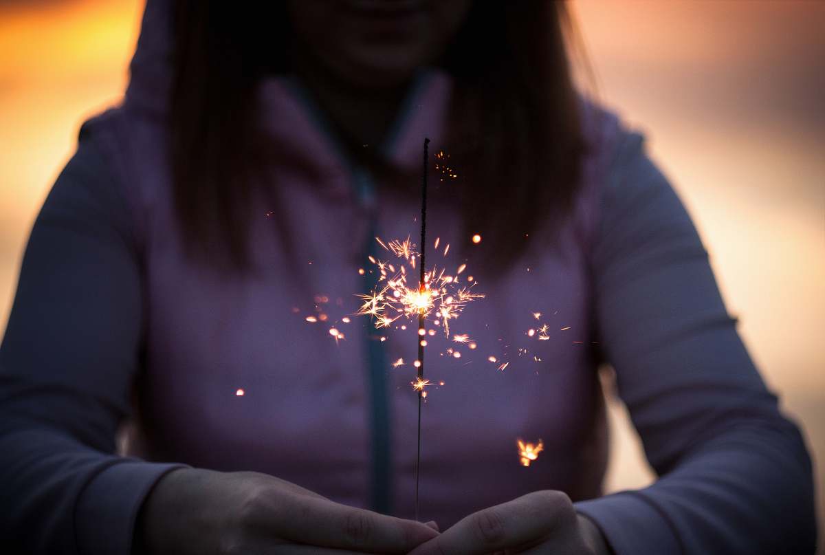 person A woman in a hoodie holds a lit sparkler in her hands light