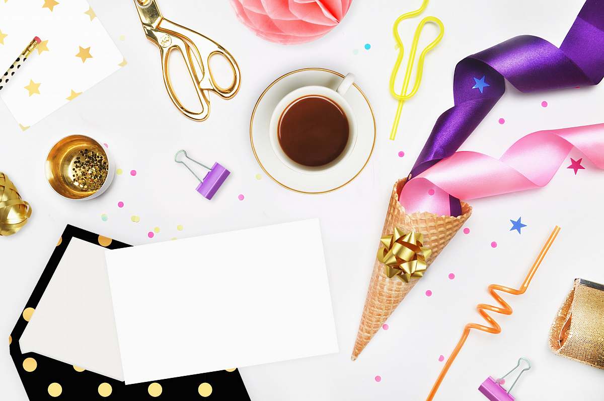 flatlay white ceramic cup filled with brown coffee on white saucer beside gold scissor straw