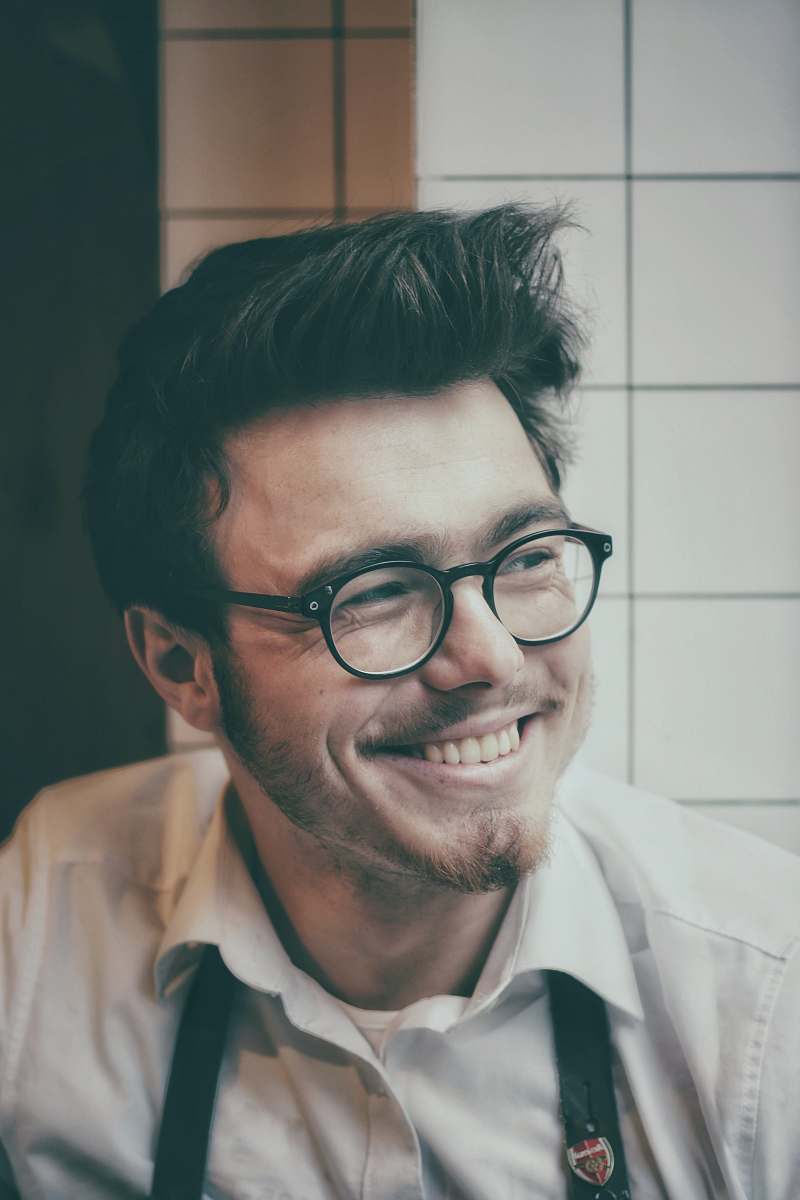 person photo of man wearing black-framed eyeglasses beside wall tile human