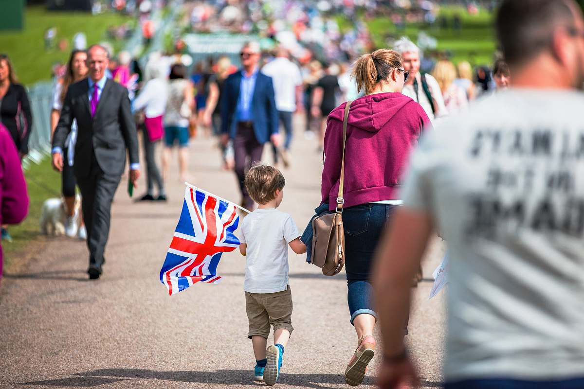 person selective focus photography of boy holding U.K. flag walking on pathway full of people human