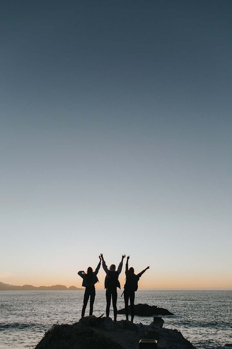 grey silhouette photography of persons raising hands while standing on island sea