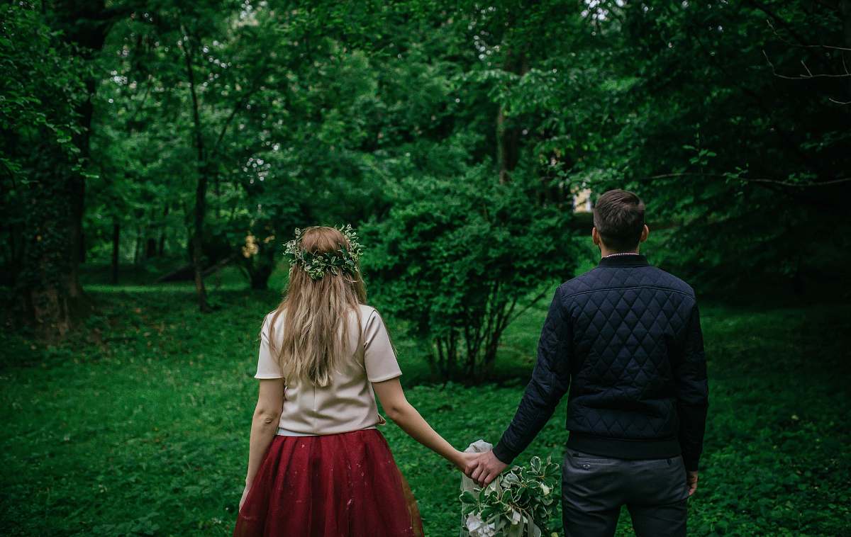 human woman and man standing holding hands facing trees back
