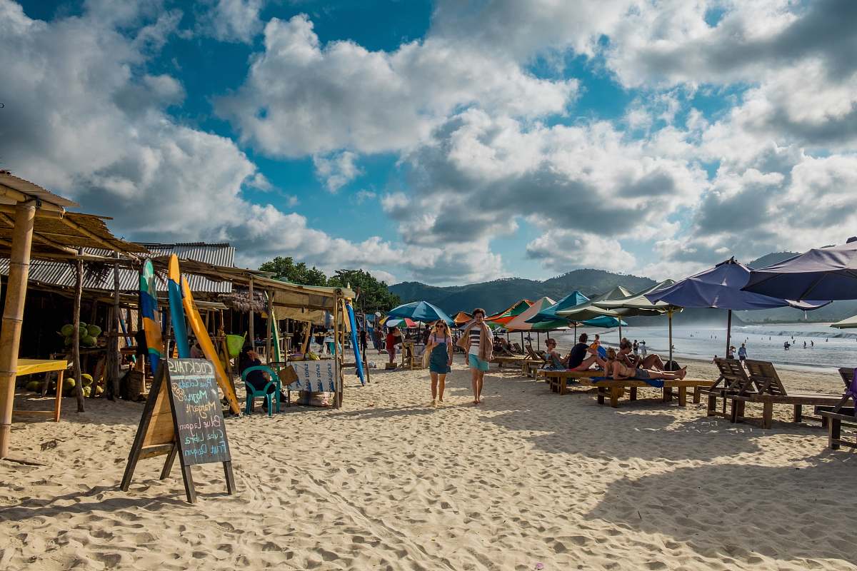 coast two person walking on beach with assorted umbrellas and nipa huts sea