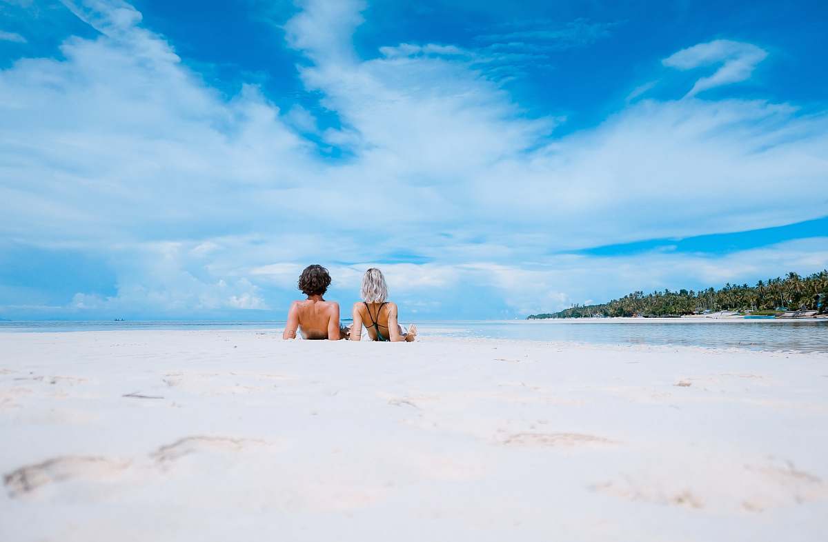 summer two women lying on white sand facing beach under blue sky water