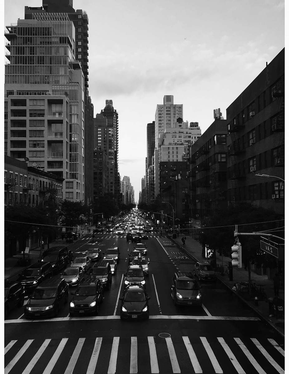 city grayscale photography of people walking on pathway near buildings and different vehicles on road road