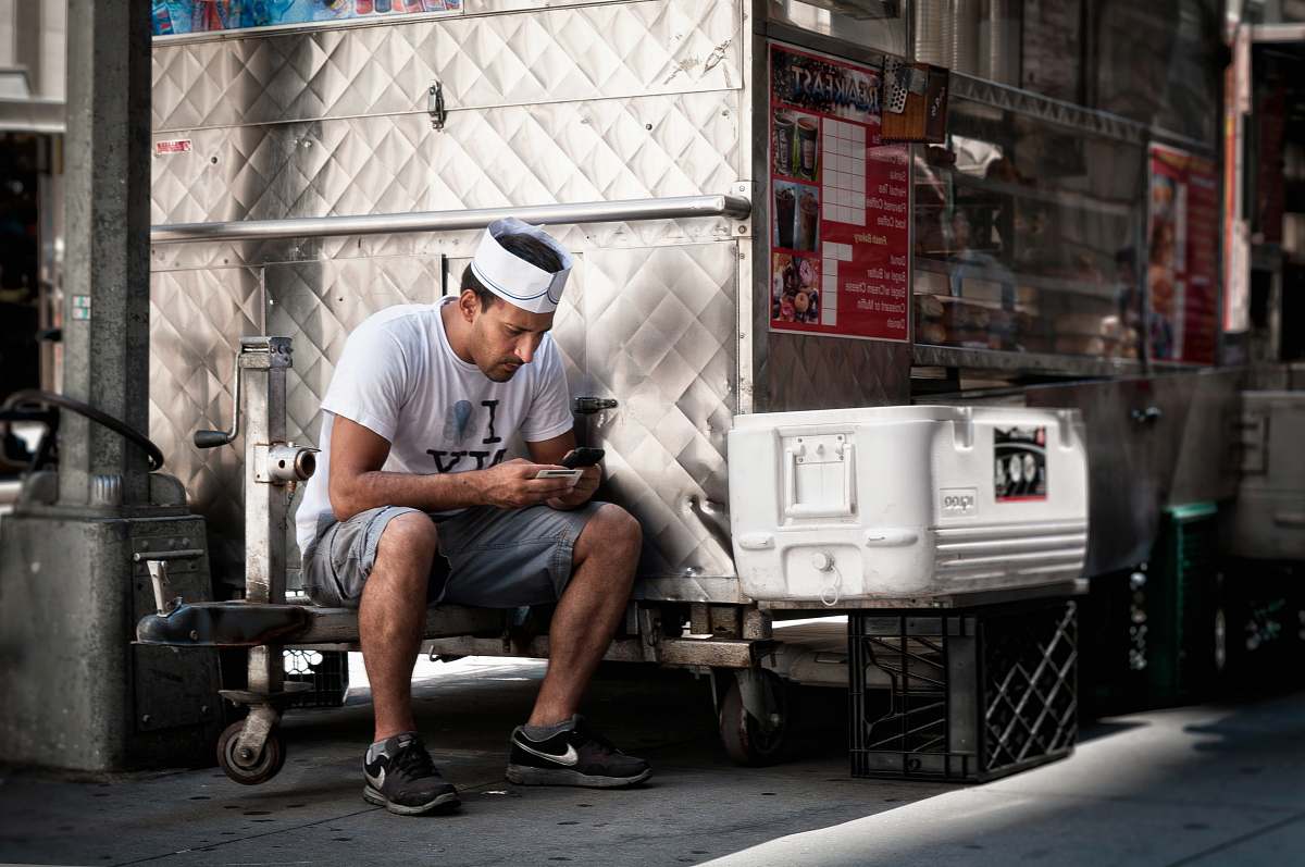 person man in white shirt holding smartphone sitting near chest cooler people