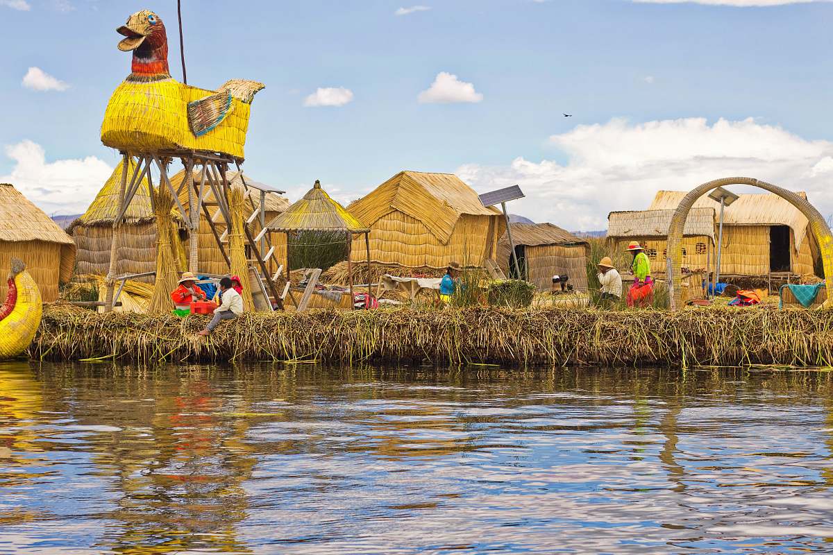 person people near brown thatched houses across river bird