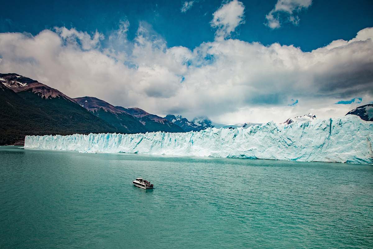 ice aerial photography of white boat on body of water beside ice block cliff during daytime mountain